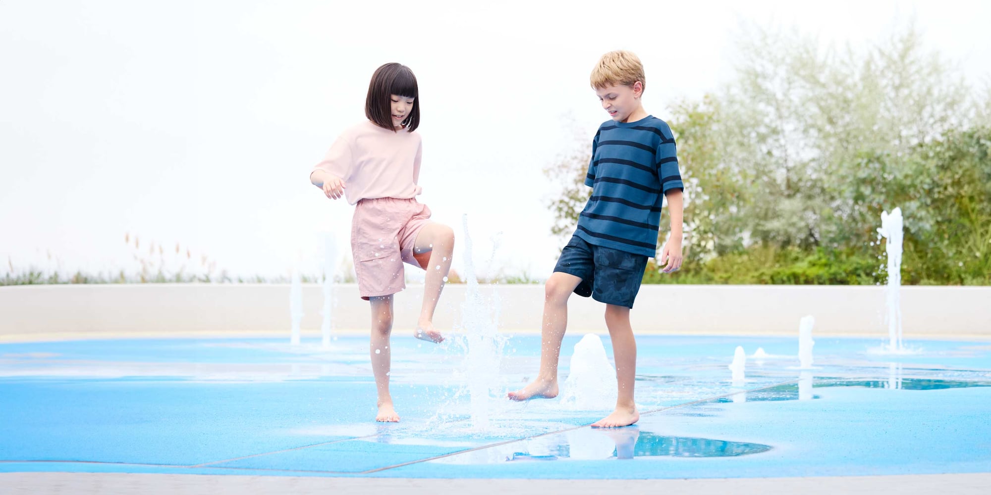 two models playing in a fountain wearing pink T-shirt and shorts and blue T-shirt and shorts