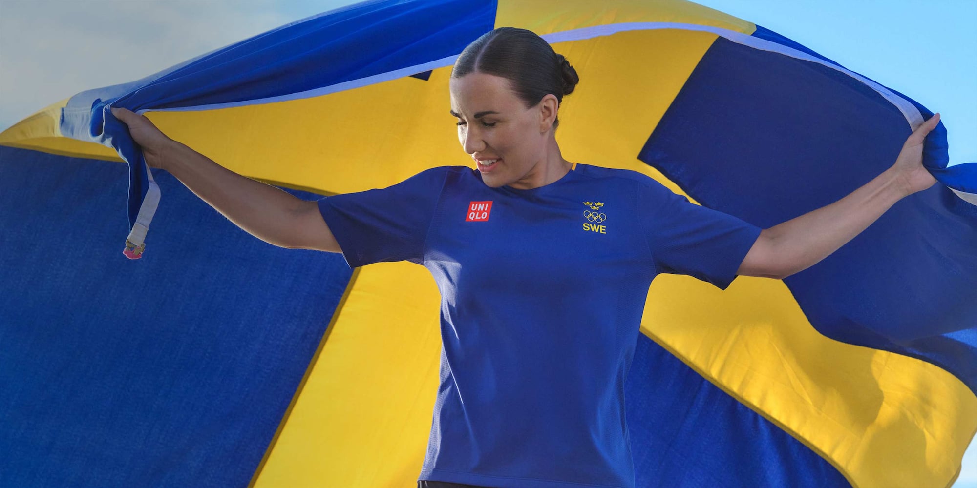 model wearing a blue t-shirt with the Sweden Olympic Team logo, holding the Swedish flag behind her