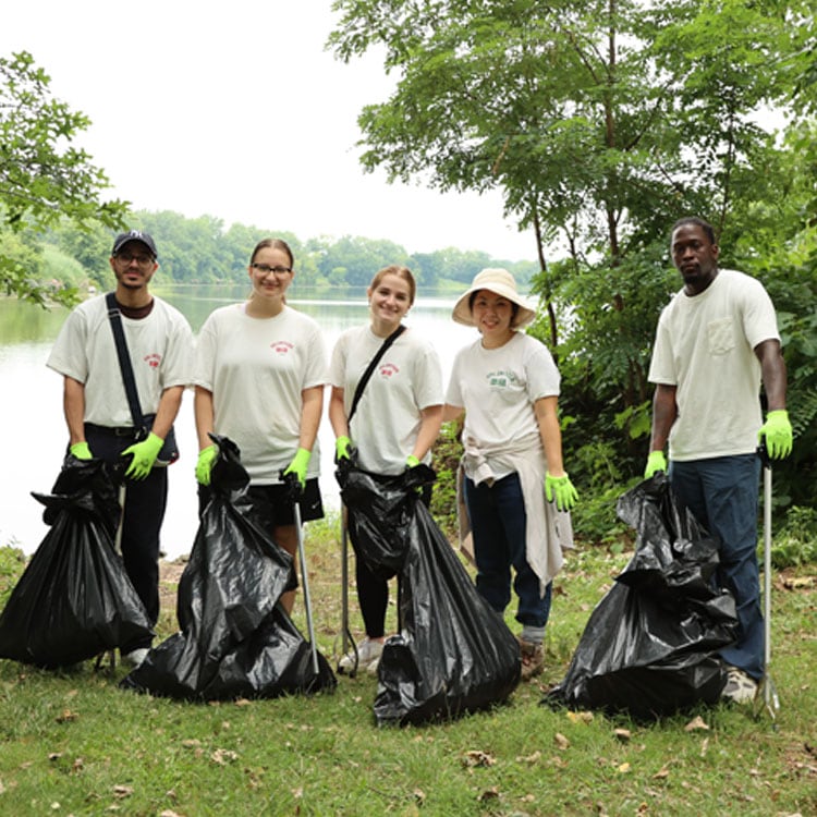 5 UNIQLO Team members participate in a cleanup with black trash bag and stick in hand at a park.