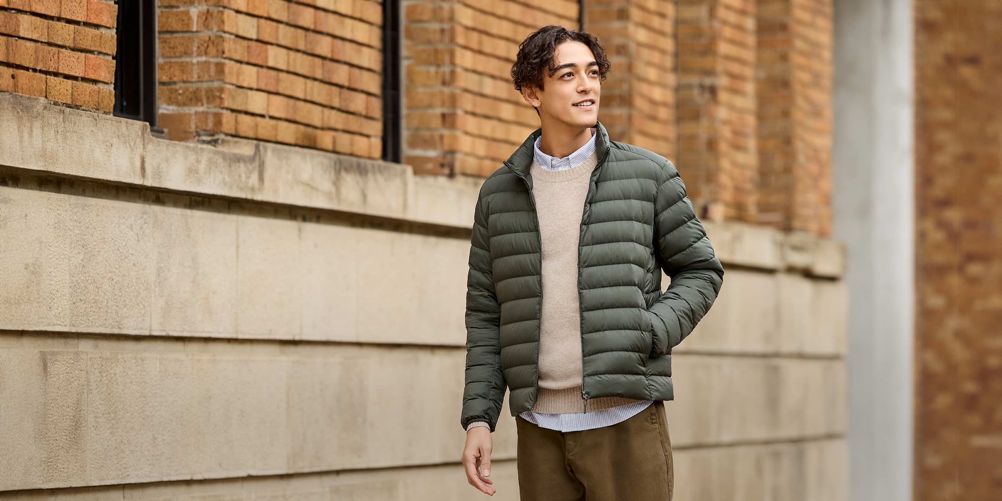 model wearing Ultra Light Down Jacket in olive over a blue and white striped shirt, beige knit and brown trousers