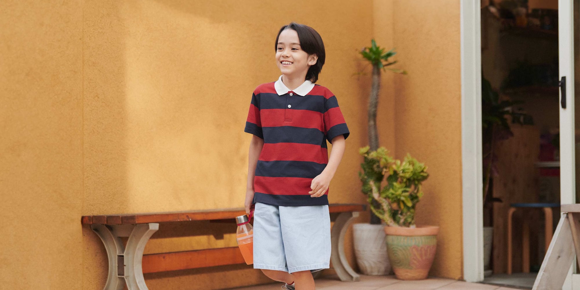 model wearing DRY Piqué Polo Shirt in red with light blue shorts, carrying a drink bottle