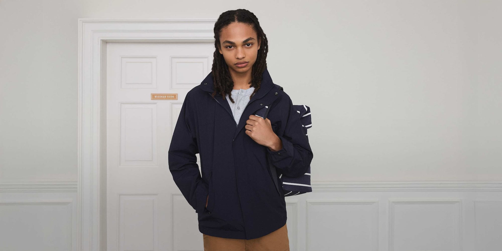 model wearing Windproof Stand Blouson in navy over a grey henley with a navy and white striped rolltop backpack