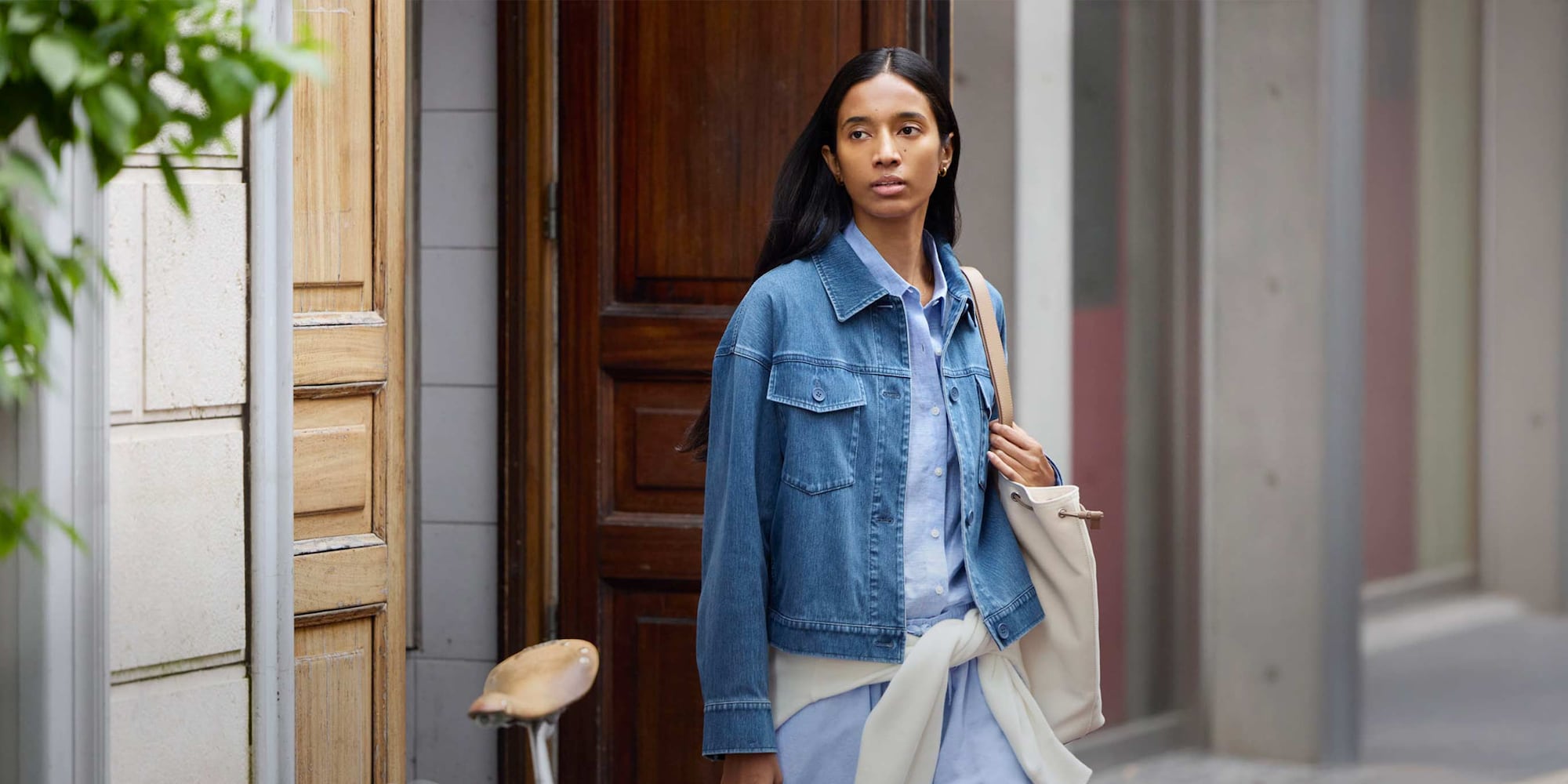 model wearing Jersey Relaxed Jacket in blue denim over a light blue shirt with an off white knit tied at the waist