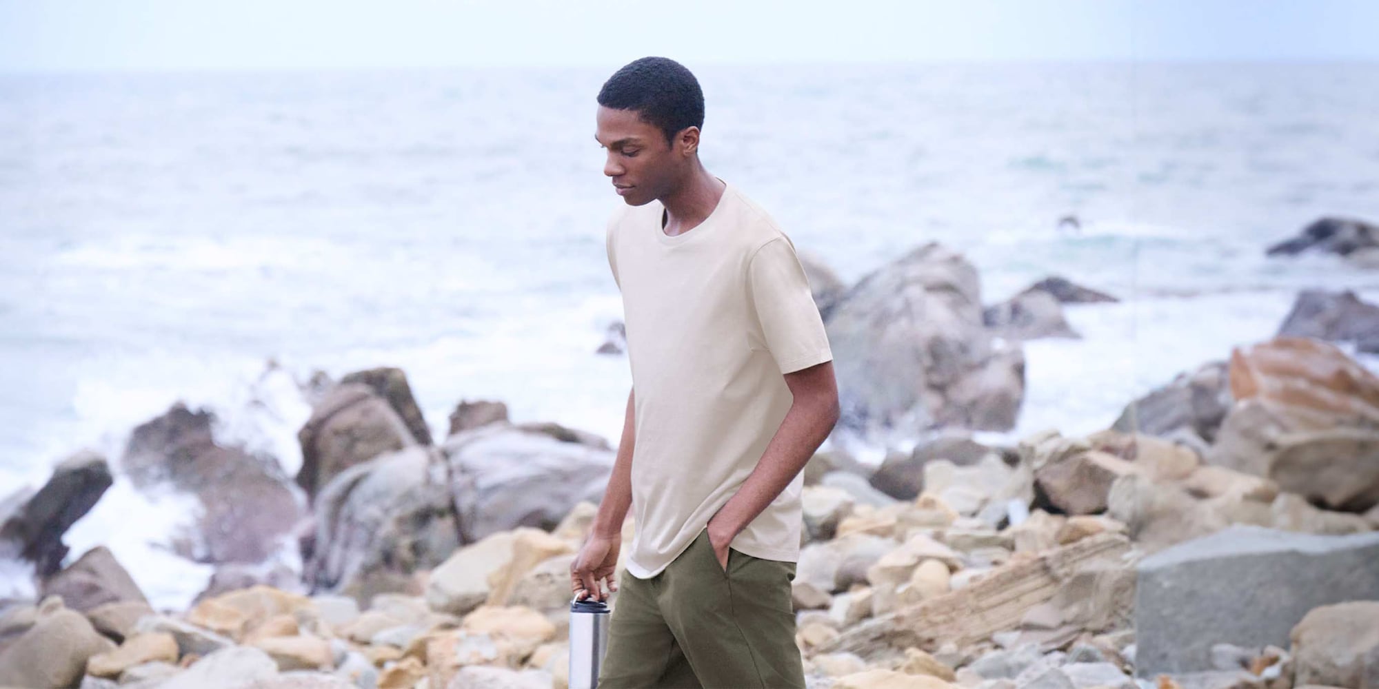 model wearing beige T-shirt and olive shorts by the sea