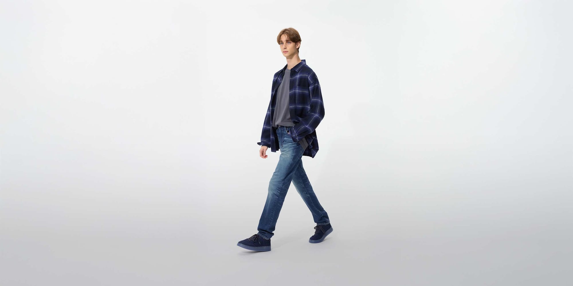 model wearing Slim Fit Jeans in blue with a navy checked shirt, grey T-shirt and navy shoes