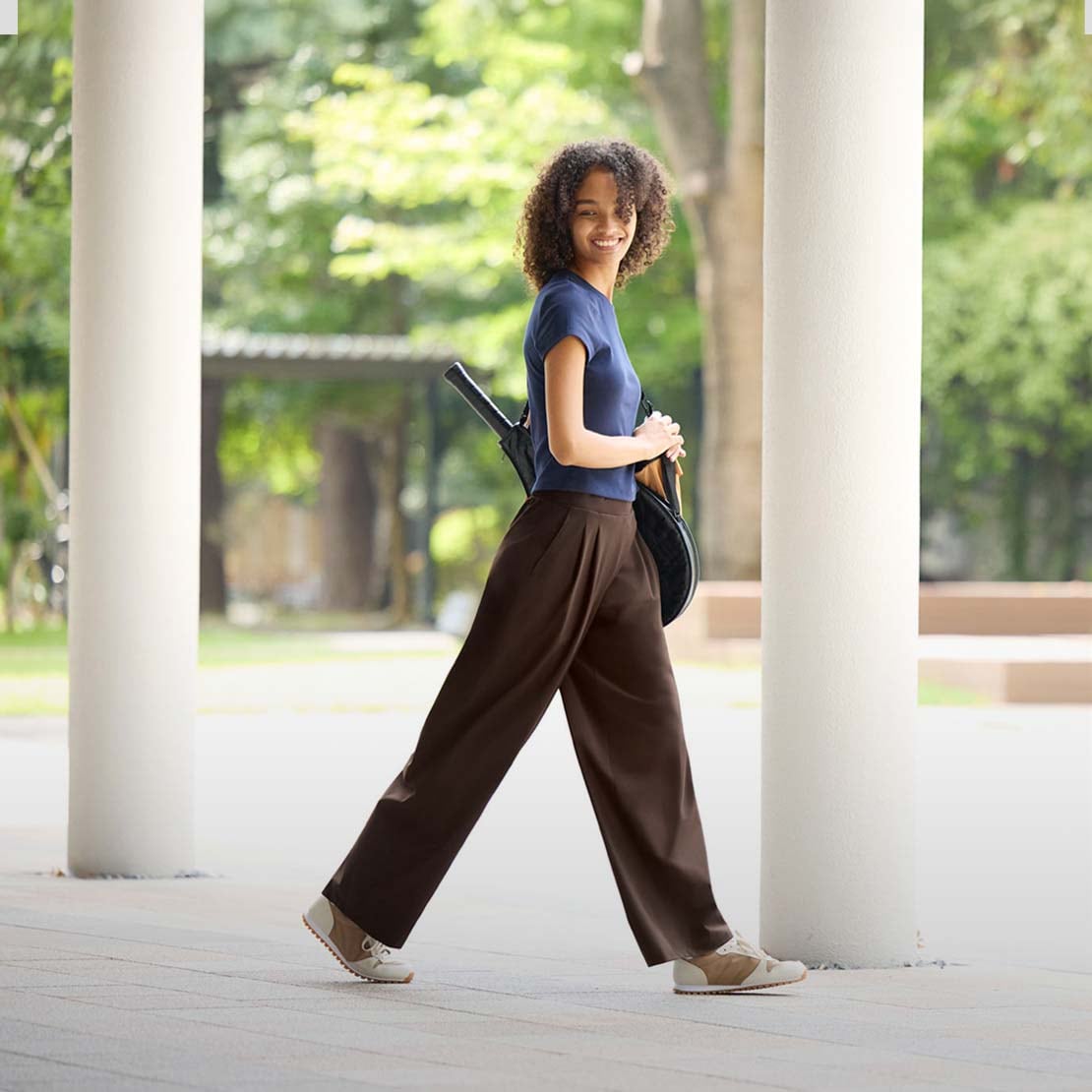 model wearing Ultra Stretch Active Wide Trousers in dark brown with a navy T-shirt while carrying a tennis racket