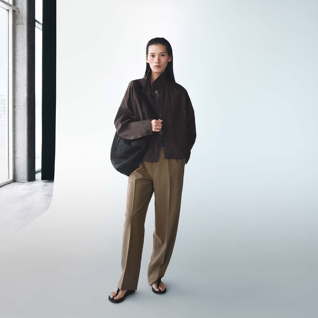 model wearing dark brown jacket, light brown trousers and a black shoulder bag