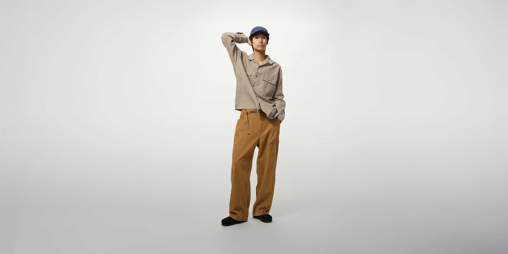 model wearing Corduroy Work Trousers in brown with a beige shirt, blue cap and black shoes