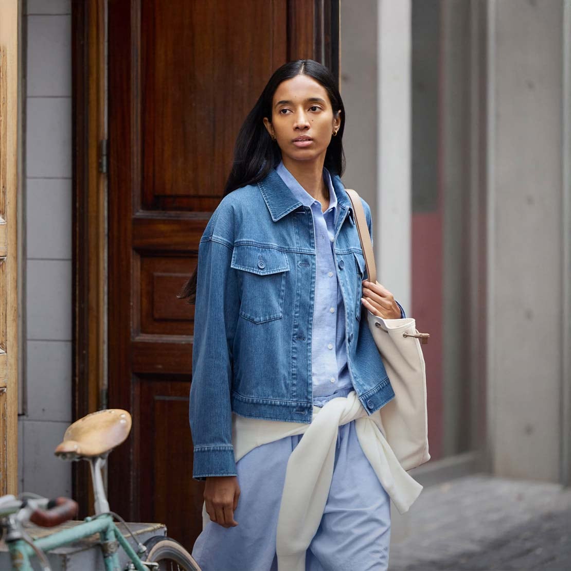 model wearing Jersey Relaxed Jacket in blue denim over a light blue shirt with an off white knit tied at the waist