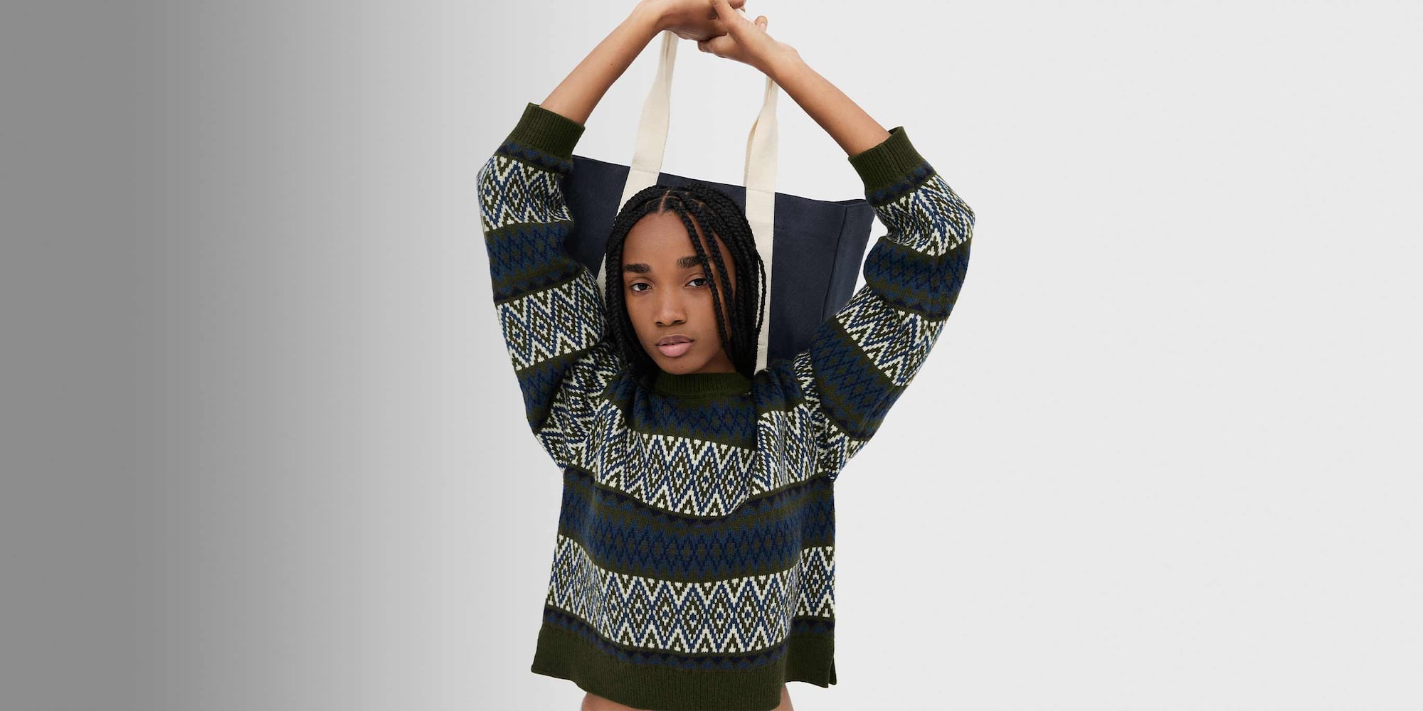 model wearing Fair Isle Crew Neck Jumper in olive while holding a canvas bag