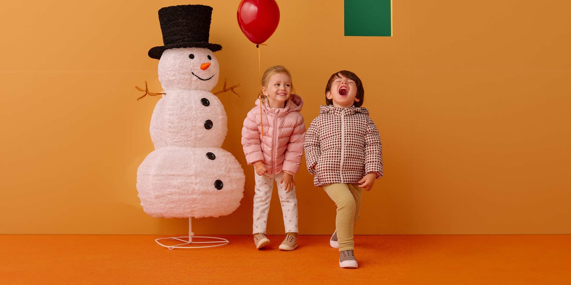 two models wearing UNIQLO leggings next to a life-sized snowman decoration