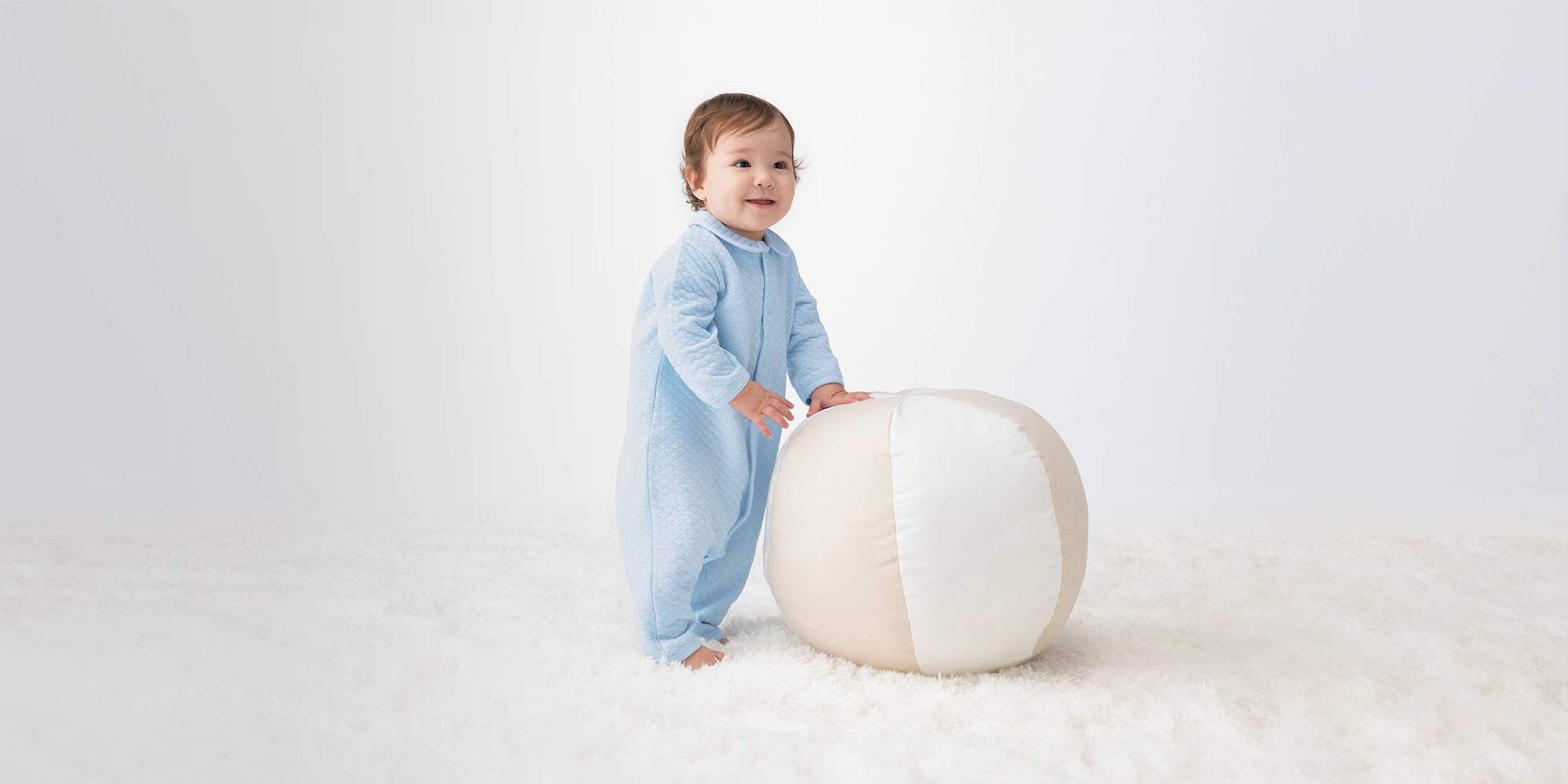 model wearing quilted onepiece outfit, in blue, stood on white rug leaning against beanbag