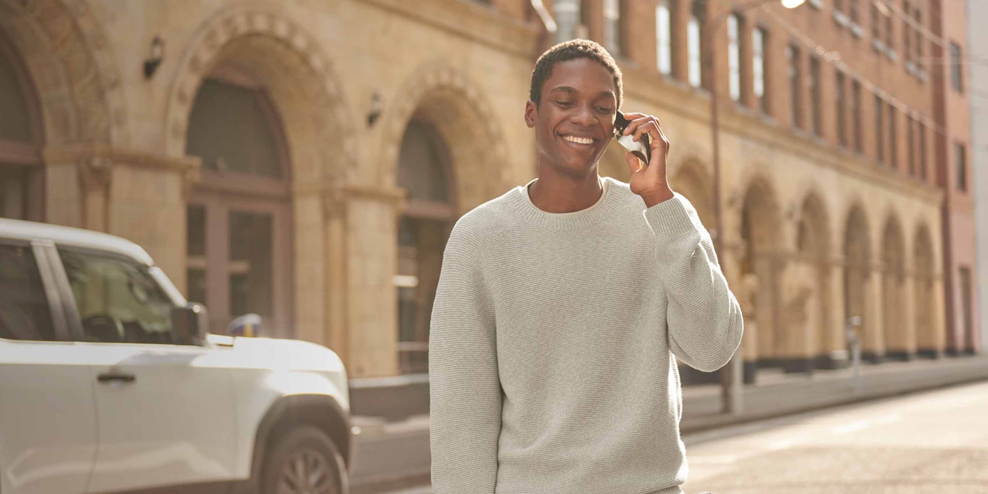 model wearing Washable 3D Knit Seamless Crew Neck Jumper in light grey while talking on a smartphone outside