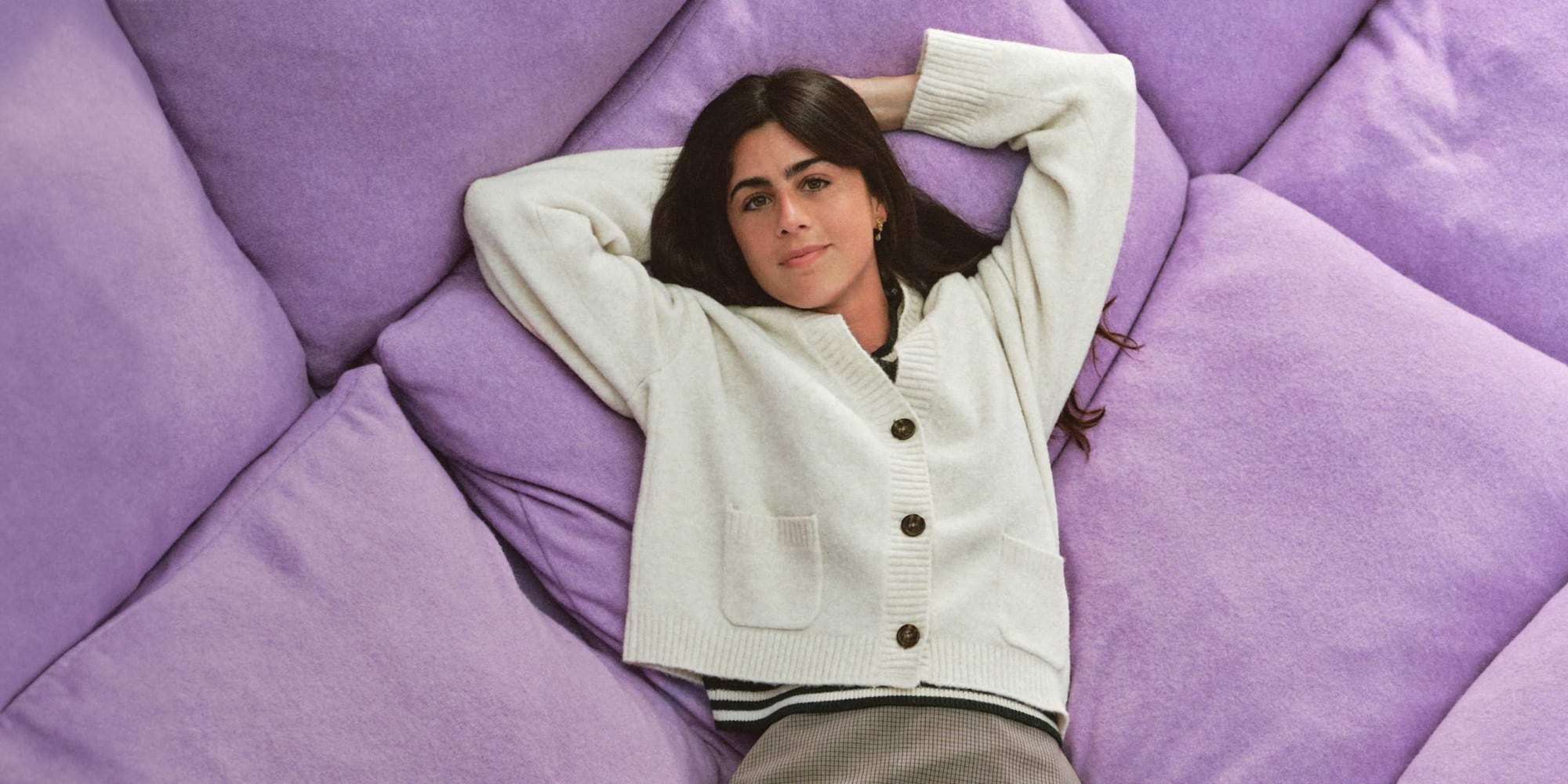 model wearing Soufflé Yarn Short Cardigan in off white while lying on a giant purple cushion