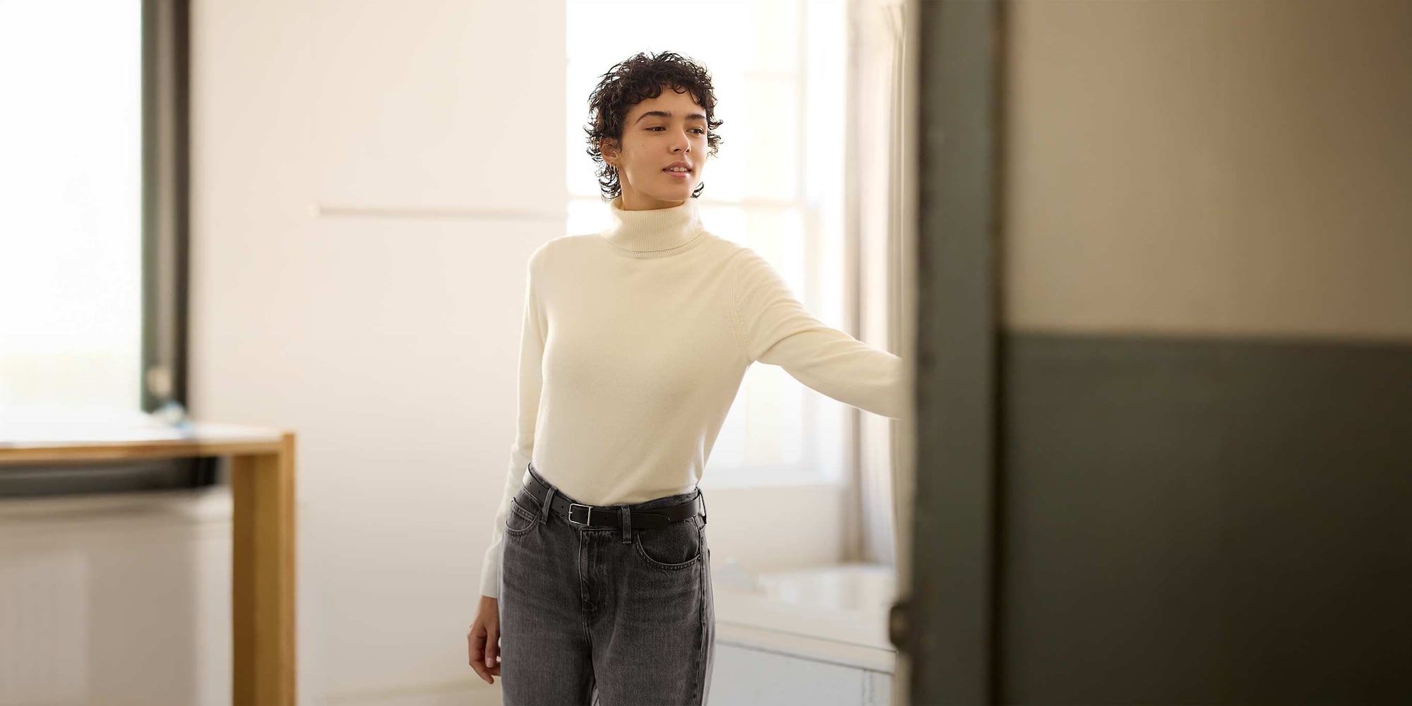 model wearing 100% Cashmere Turtleneck Jumper in off white with grey jeans and a black belt